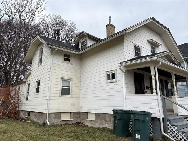 view of property exterior with a chimney, covered porch, and a lawn