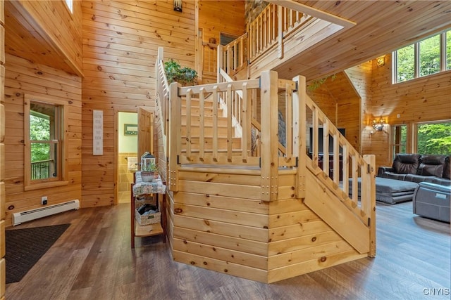 stairs with wood walls, a baseboard radiator, wood finished floors, and a towering ceiling