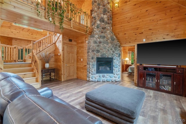 living area with wooden walls, high vaulted ceiling, wood finished floors, stairs, and a stone fireplace