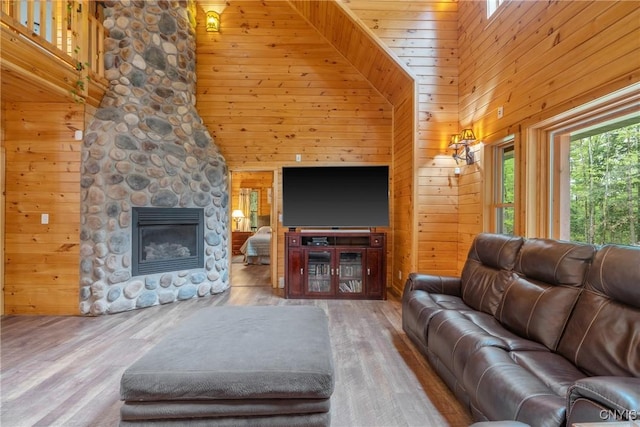 living room featuring wooden walls, a high ceiling, a stone fireplace, and wood finished floors