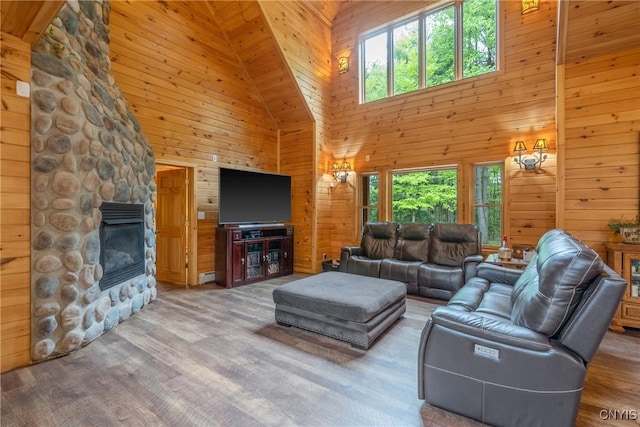 living room with high vaulted ceiling, wood walls, plenty of natural light, a fireplace, and wood finished floors