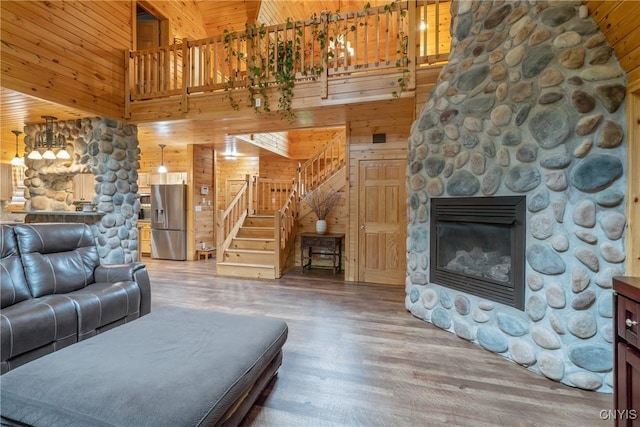living area featuring wood walls, a high ceiling, wood finished floors, stairs, and a stone fireplace