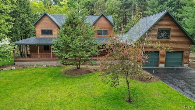 cabin with driveway, a front yard, a porch, a shingled roof, and a view of trees