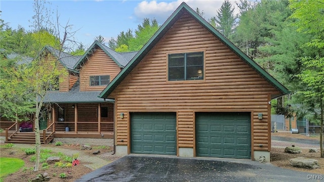 view of front of house with an attached garage, a porch, driveway, roof with shingles, and log veneer siding