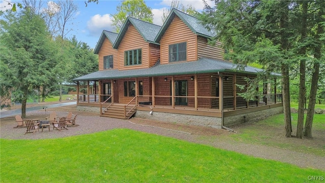 rear view of property featuring an outdoor fire pit, faux log siding, covered porch, a lawn, and roof with shingles