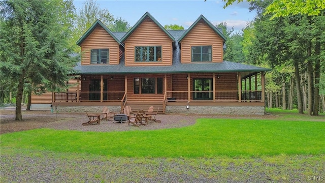 rear view of house with an outdoor fire pit, a lawn, a porch, roof with shingles, and log veneer siding