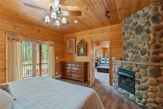 bedroom featuring access to exterior, baseboard heating, wood finished floors, a stone fireplace, and wooden walls
