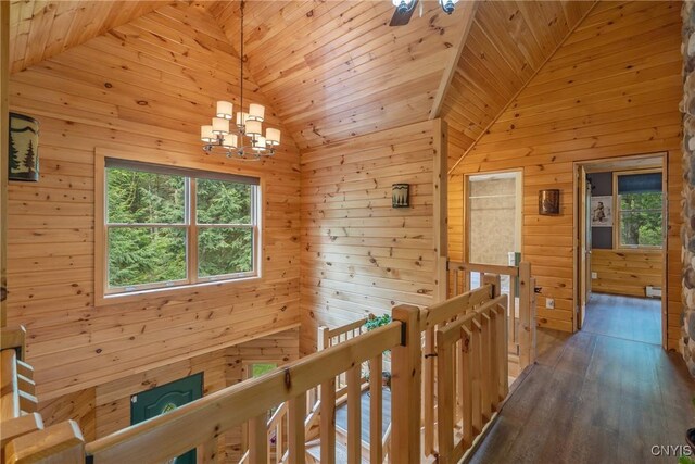 corridor with lofted ceiling, a chandelier, an upstairs landing, wood walls, and wooden ceiling