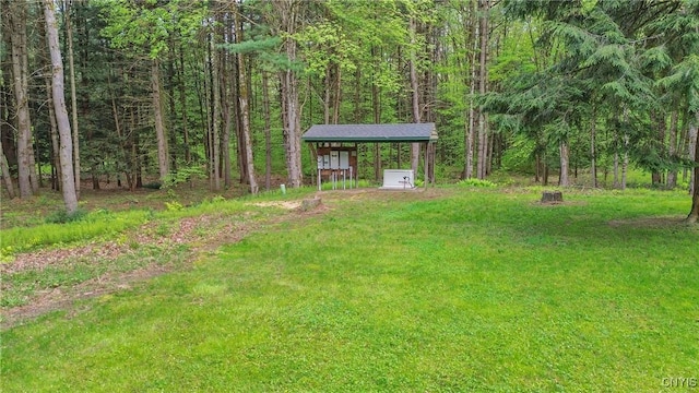 view of green lawn featuring a detached carport and a forest view
