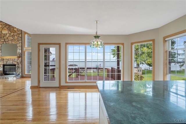 7179 Lakeshore Rd, Cicero, NY 13039 - unfurnished dining area with light wood-type flooring, a fireplace, and a chandelier