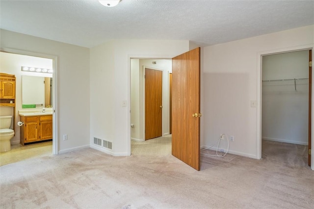 unfurnished bedroom with a spacious closet, light carpet, a closet, baseboards, and a textured ceiling