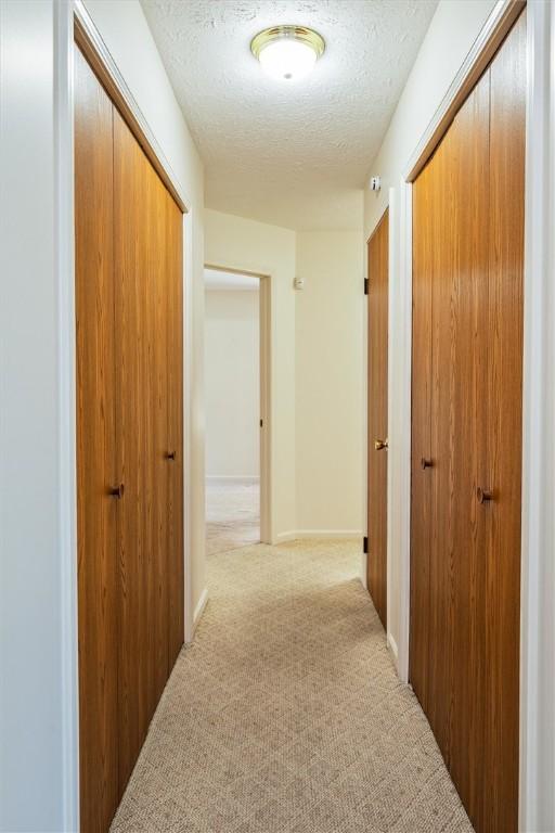 hallway featuring light carpet and a textured ceiling