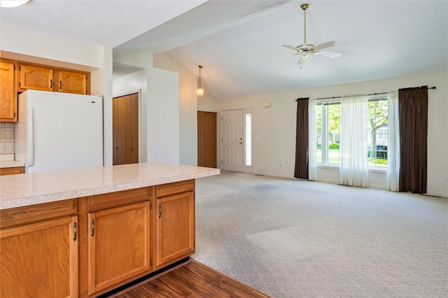 kitchen with freestanding refrigerator, vaulted ceiling, light countertops, brown cabinetry, and a ceiling fan