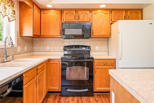 kitchen with black appliances, a sink, wood finished floors, light countertops, and recessed lighting