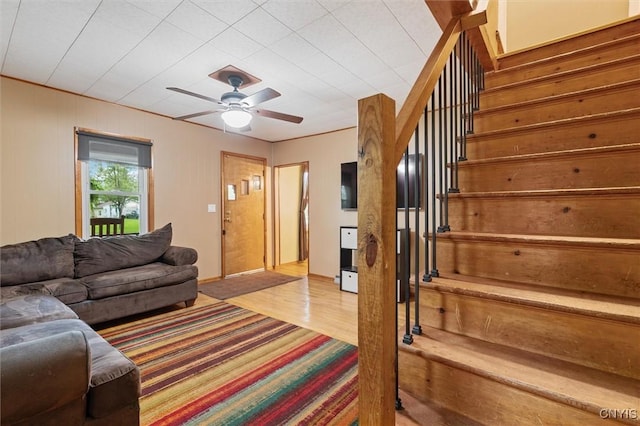 living room with stairs, light wood-type flooring, and a ceiling fan