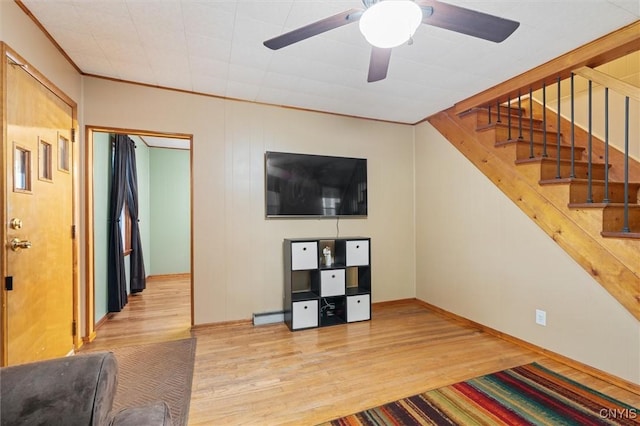 unfurnished living room featuring wood finished floors, baseboards, stairway, ceiling fan, and crown molding