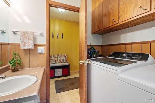 clothes washing area featuring washer and dryer, wood walls, a wainscoted wall, cabinet space, and light tile patterned floors