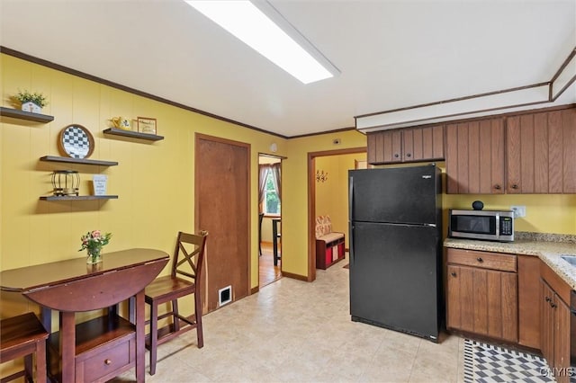 kitchen with freestanding refrigerator, stainless steel microwave, open shelves, brown cabinetry, and crown molding