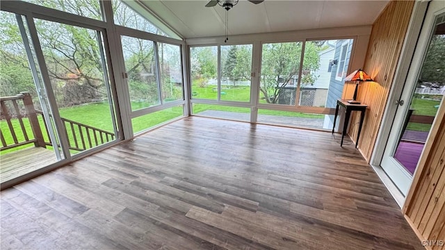 unfurnished sunroom featuring ceiling fan, a wooden deck, wood finished floors, and lofted ceiling