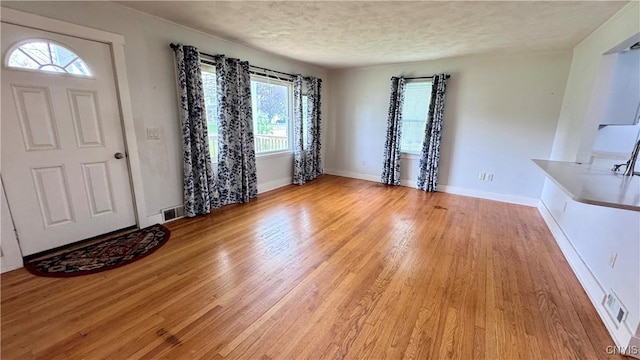 foyer entrance with light wood finished floors, a textured ceiling, and baseboards