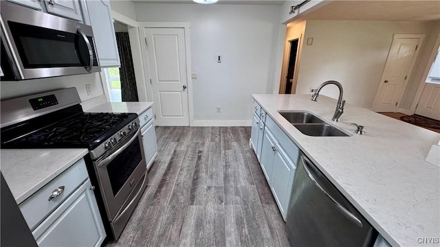 kitchen with appliances with stainless steel finishes, a sink, dark wood finished floors, and baseboards