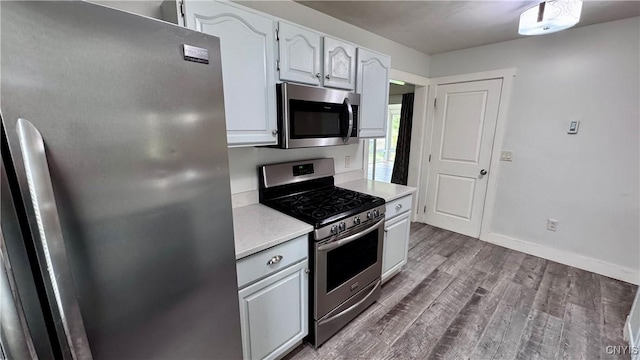 kitchen featuring stainless steel appliances, light countertops, wood finished floors, baseboards, and white cabinetry