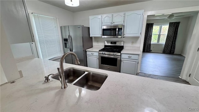 kitchen with stainless steel appliances, a sink, ceiling fan, white cabinetry, and baseboards