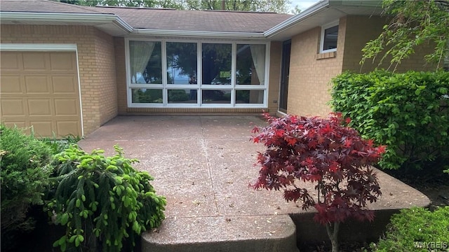 view of exterior entry with brick siding, a garage, and roof with shingles