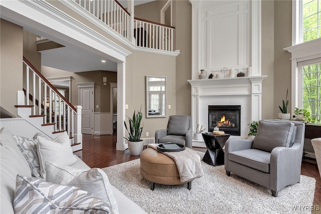 living room featuring wood finished floors, a high ceiling, a tile fireplace, stairs, and baseboards