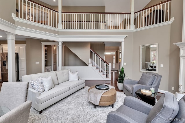 living area with decorative columns, a high ceiling, stairway, and baseboards