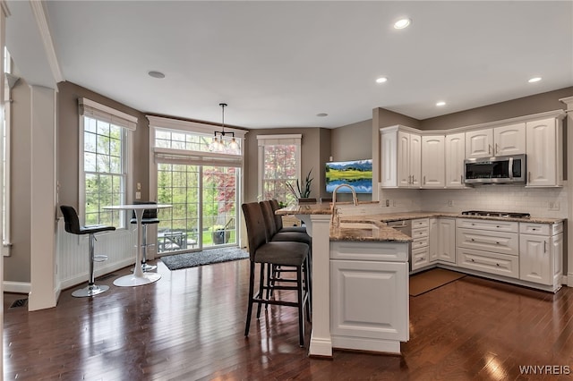 kitchen with stainless steel appliances, a sink, dark wood-style flooring, a peninsula, and white cabinets