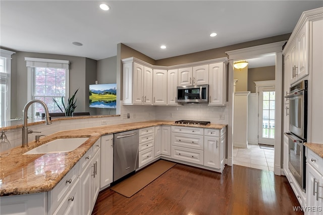 kitchen with stainless steel appliances, a sink, dark wood-style floors, white cabinetry, and tasteful backsplash