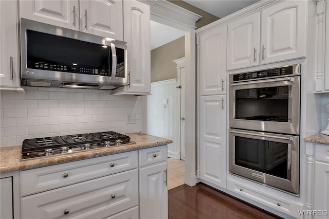 kitchen featuring appliances with stainless steel finishes, white cabinets, decorative backsplash, and light stone countertops