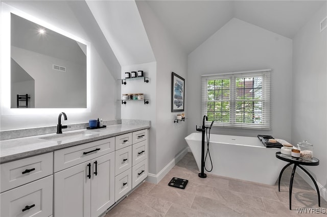 full bath featuring vaulted ceiling, a freestanding tub, vanity, and baseboards