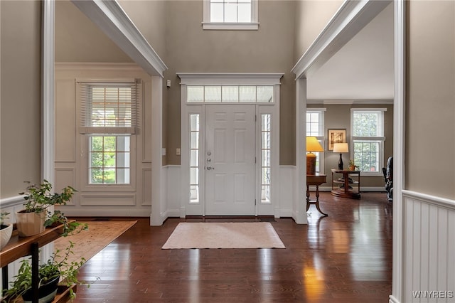 entrance foyer with a decorative wall, wainscoting, a high ceiling, wood finished floors, and ornamental molding