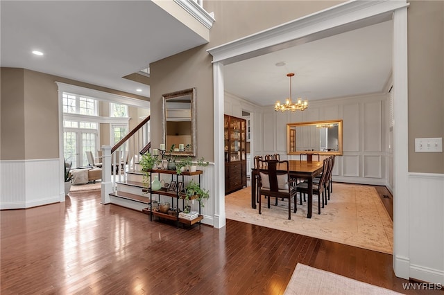 dining room with a decorative wall, a chandelier, wood finished floors, stairs, and wainscoting