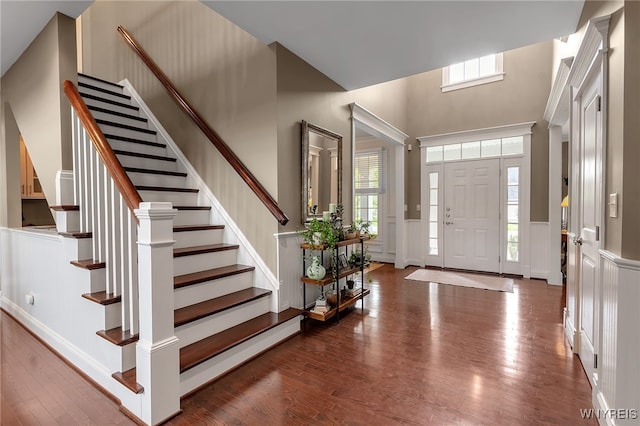 foyer featuring wood finished floors, stairs, a decorative wall, and a wainscoted wall
