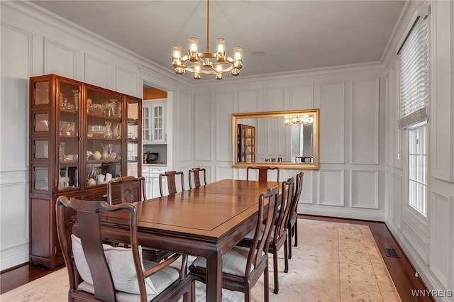 dining room featuring a decorative wall, a chandelier, wood finished floors, and ornamental molding