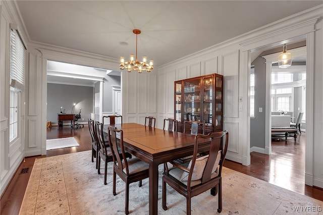 dining area featuring a decorative wall, ornamental molding, light wood-style floors, a chandelier, and decorative columns
