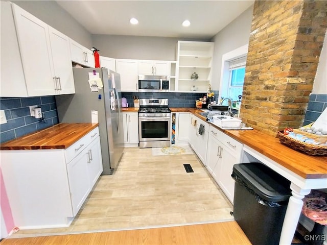 kitchen with wood counters, stainless steel appliances, a sink, open shelves, and white cabinets