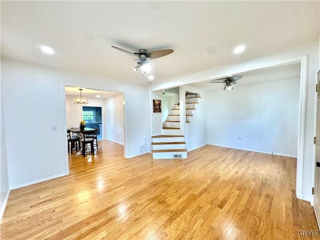 unfurnished room featuring stairs, light wood-style flooring, a ceiling fan, a chandelier, and baseboards