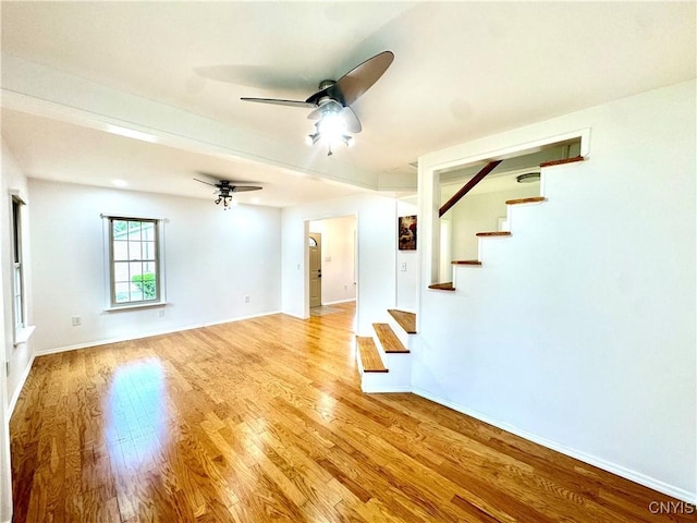 unfurnished living room with stairs, ceiling fan, light wood-style flooring, and baseboards