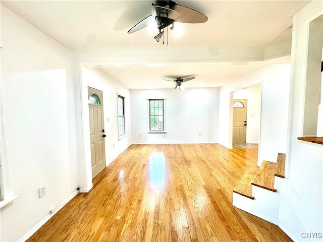 unfurnished living room with a ceiling fan, light wood-style flooring, baseboards, and stairs