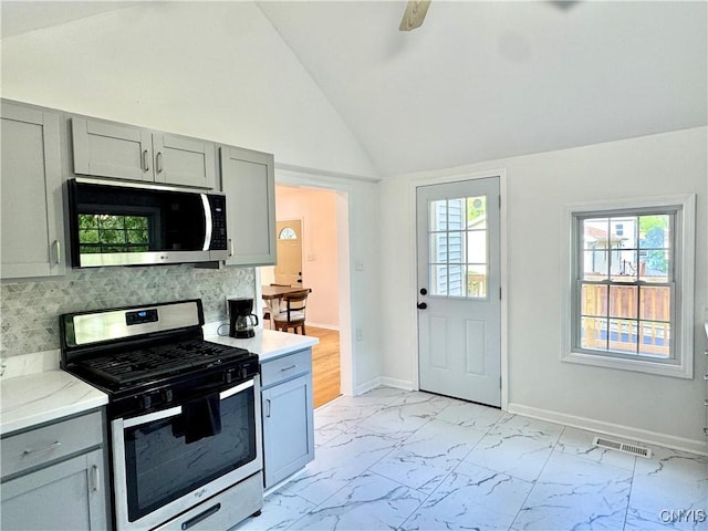 kitchen featuring appliances with stainless steel finishes, gray cabinetry, light marble finish floors, vaulted ceiling, and tasteful backsplash