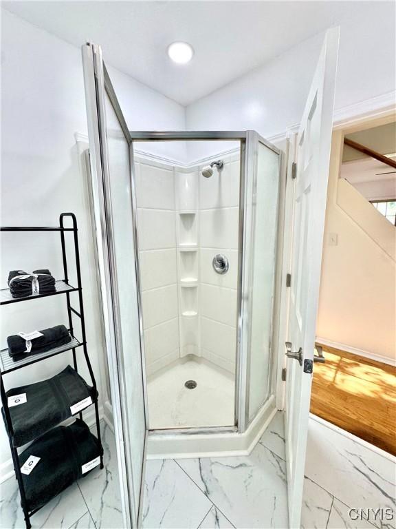 bathroom with marble finish flooring, a stall shower, and baseboards