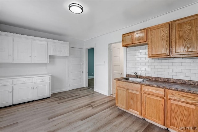 kitchen with a sink, tasteful backsplash, light wood-style floors, dark countertops, and white cabinets