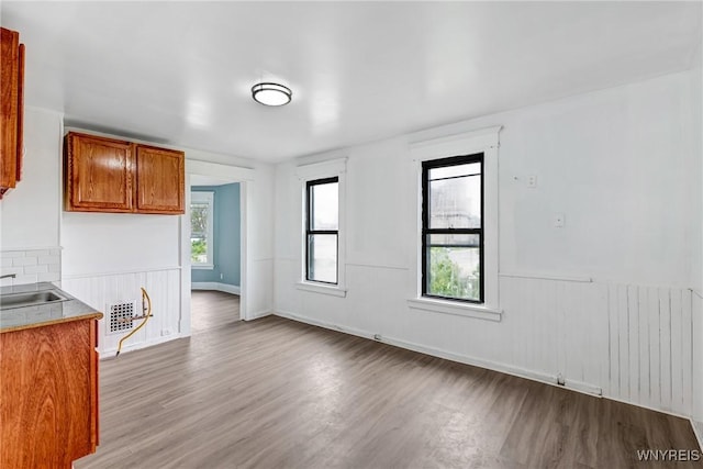 kitchen featuring wood finished floors, wainscoting, brown cabinets, light countertops, and open floor plan