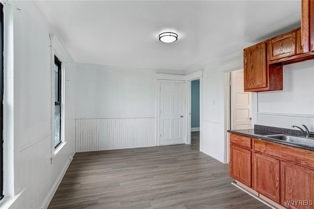 kitchen with a sink, dark countertops, wood finished floors, and brown cabinets