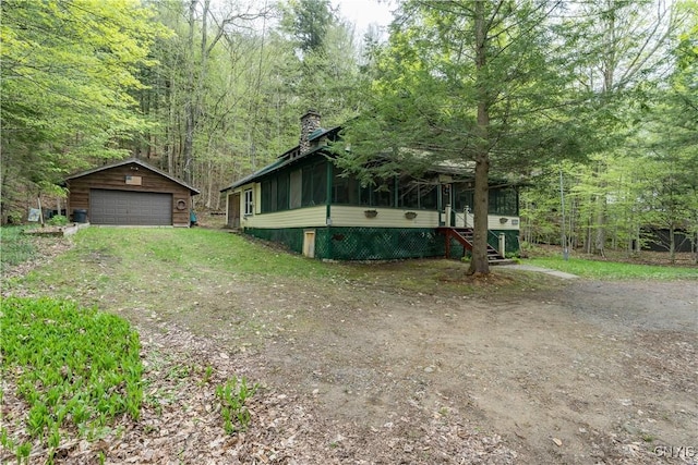 view of front of home with a detached garage, an outbuilding, a chimney, a sunroom, and a wooded view