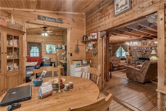dining space featuring wood walls, ceiling fan, wooden ceiling, lofted ceiling, and a fireplace